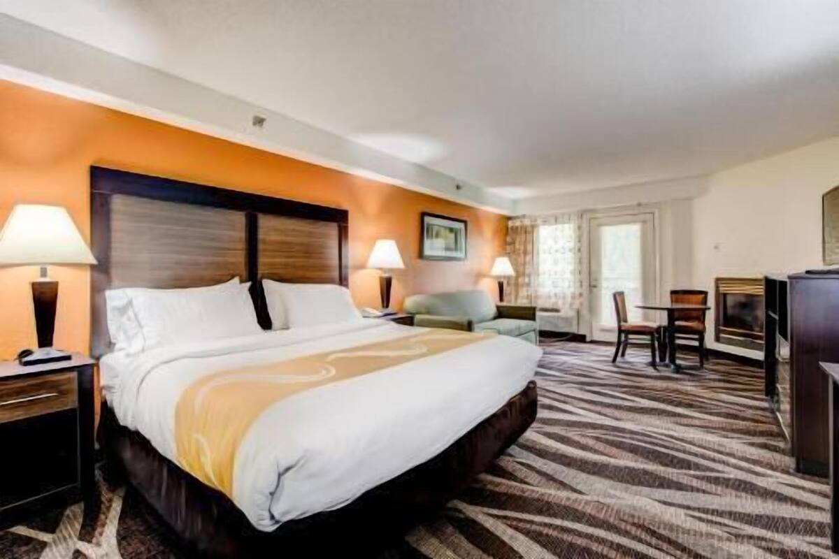 Habitación de hotel con una cama grande, dos mesitas de noche con lámparas, un pequeño sofá, un escritorio con sillas y una chimenea.