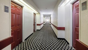 A hotel corridor with checkered carpet, red doors, and numbered room signs. - Red Roof Inn & Suites Mobile SW – I-10 (Mobile)