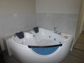 A large, white, freestanding bathtub with a blue interior, positioned in a corner of a room with tiled walls and wooden flooring.
