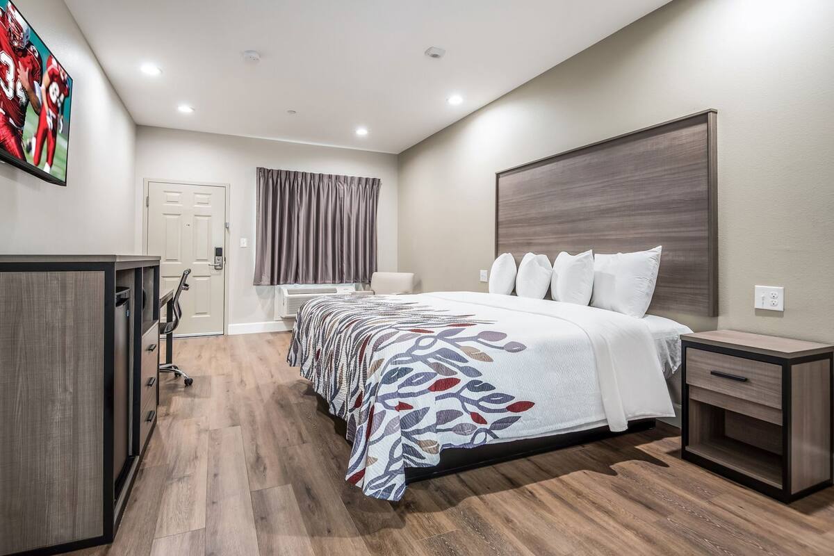 A modern hotel room with a large bed, a desk, a chair, and a wardrobe.