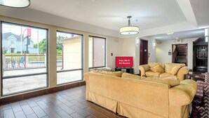 Un salon spacieux avec un grand canapé, un téléviseur à écran plat et une vue sur un quartier résidentiel grâce à de grandes fenêtres.