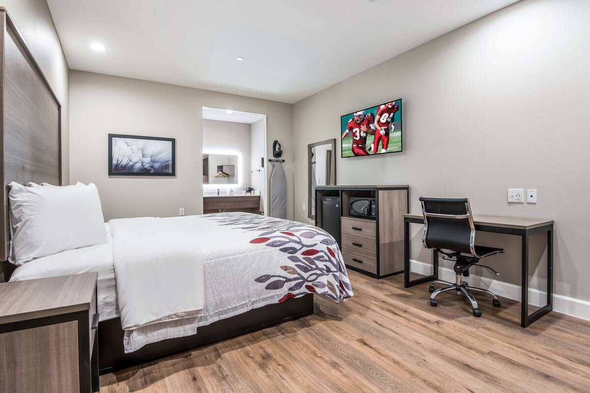 A modern bedroom with a bed, desk, chair, and a TV mounted on the wall.