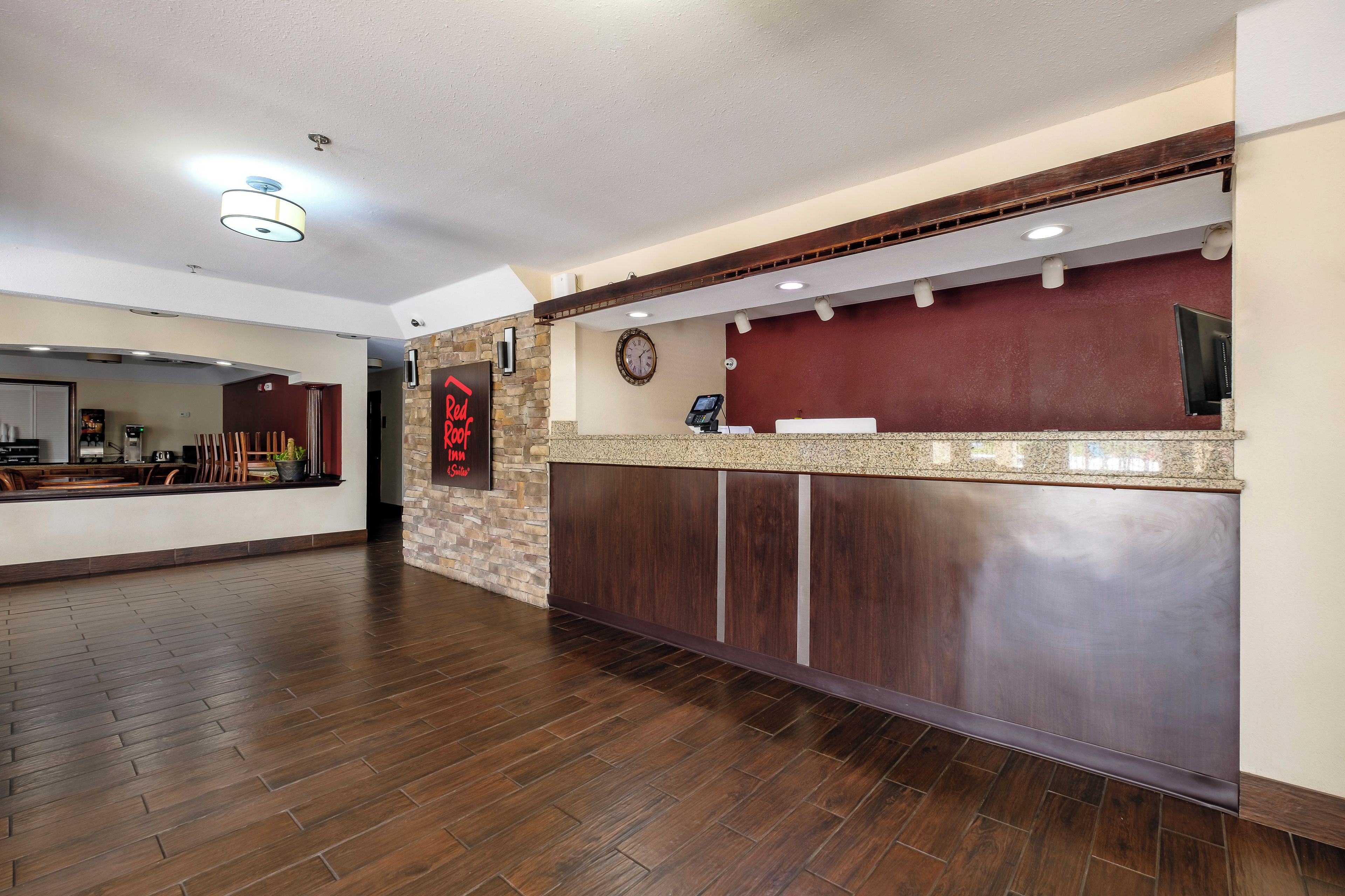A hotel reception area with a wooden reception desk, a clock, and a digital phone.