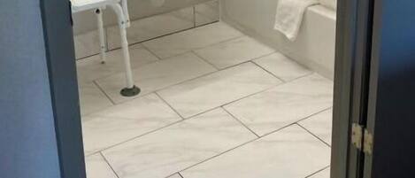 Un baño pequeño con lavamanos, espejo, ducha con cortina y una silla blanca.
