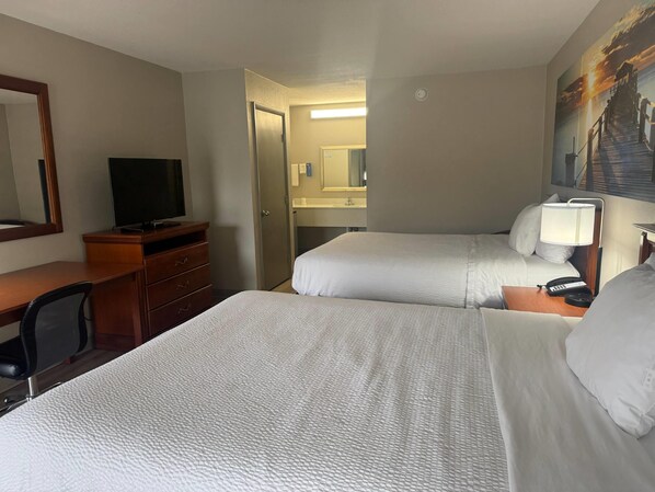 Habitación de hotel con dos camas, un escritorio con silla, televisión, lámpara de escritorio y un cuadro en la pared.