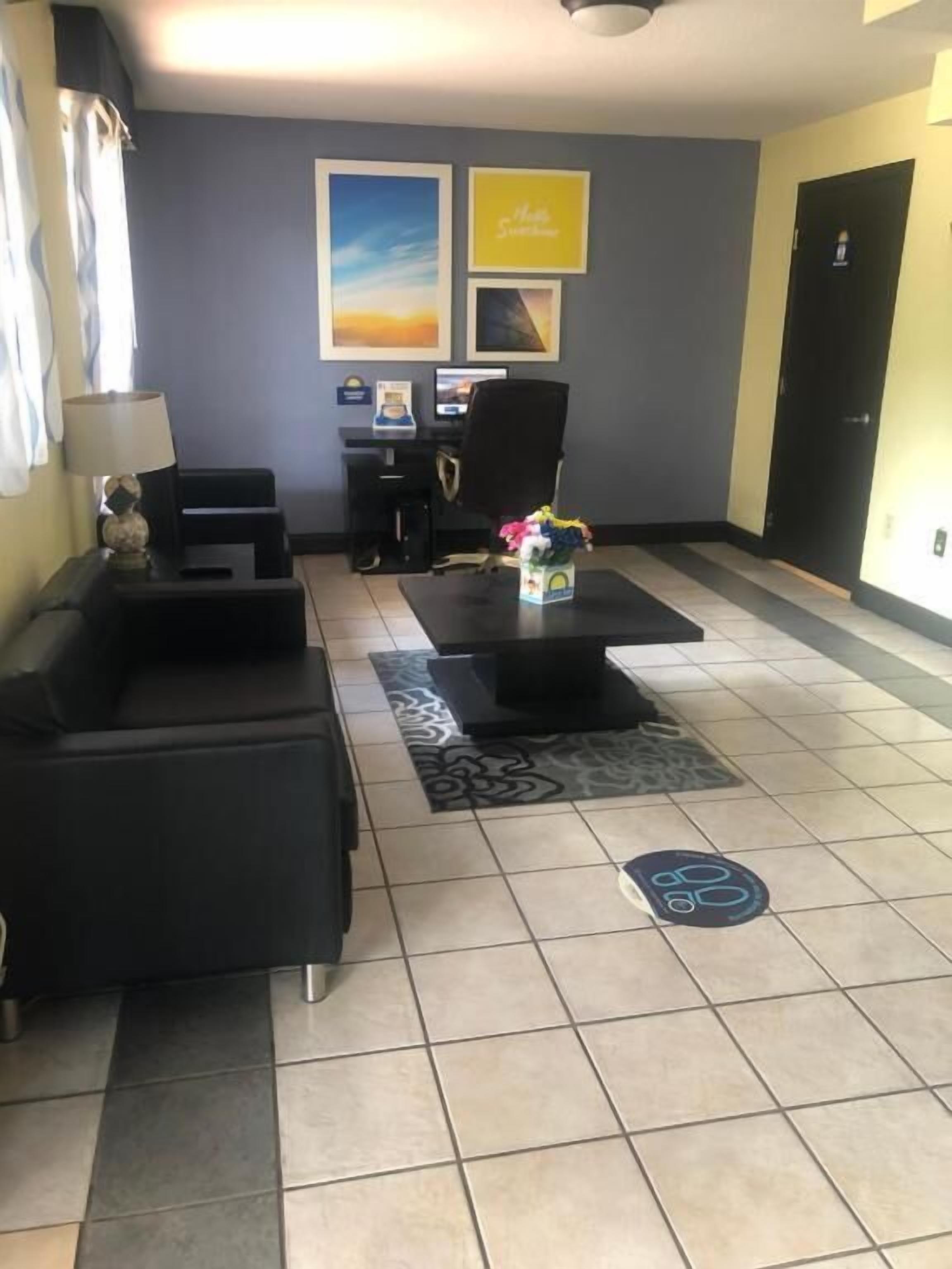 Un vestíbulo de hotel con un mostrador de recepción, dos sofás negros, una mesa de centro y una alfombra.
