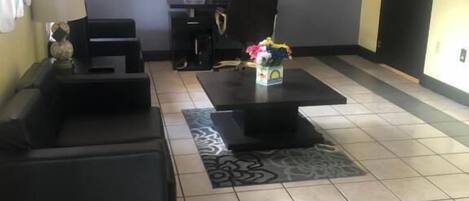 Un vestíbulo de hotel con un mostrador de recepción, dos sofás negros, una mesa de centro y una alfombra.