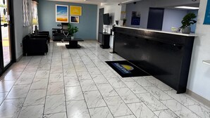 Una recepción con mostrador negro, escritorio, silla, planta en maceta y una puerta.
