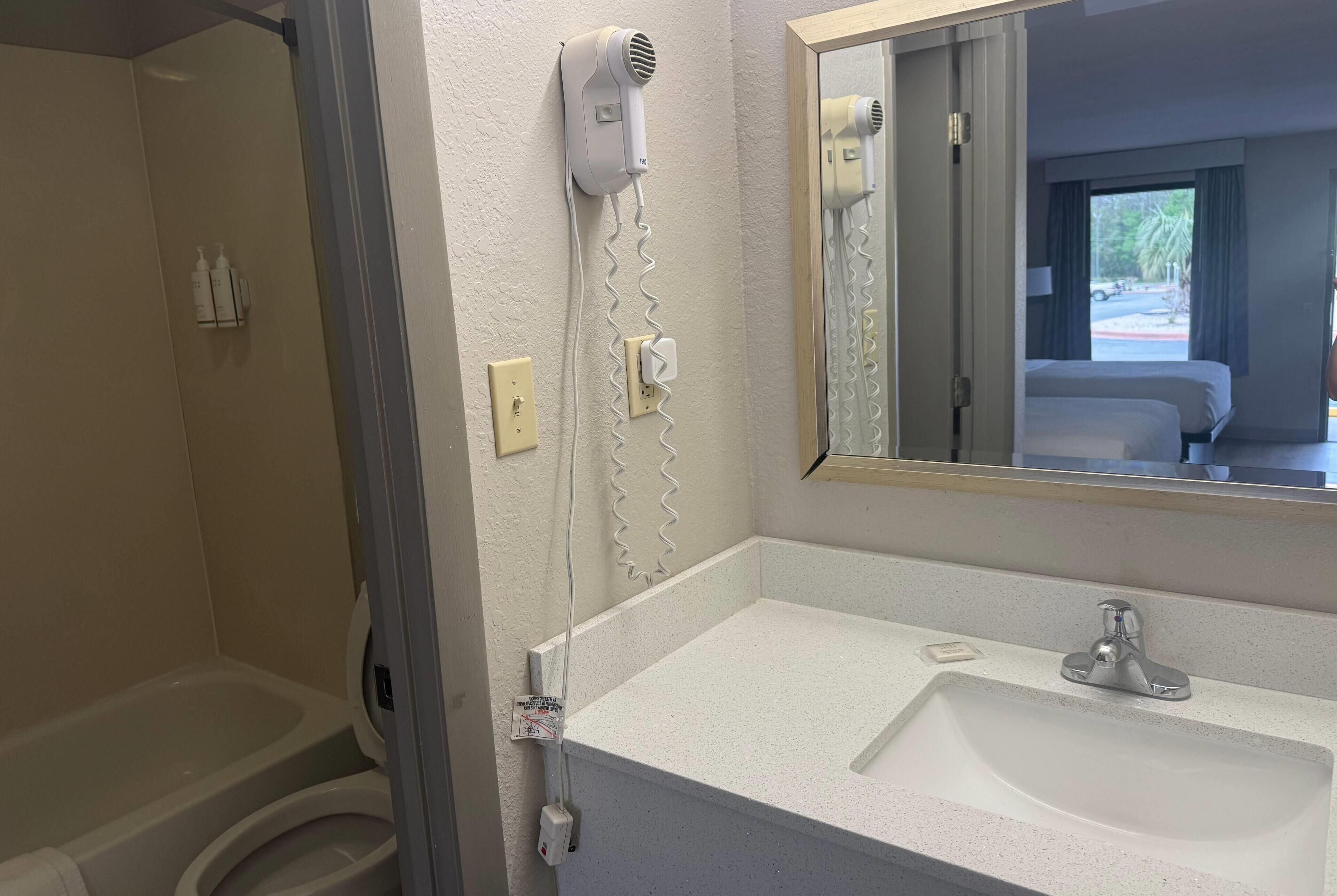 Un baño con lavamanos blanco, espejo, secador de pelo y ducha.