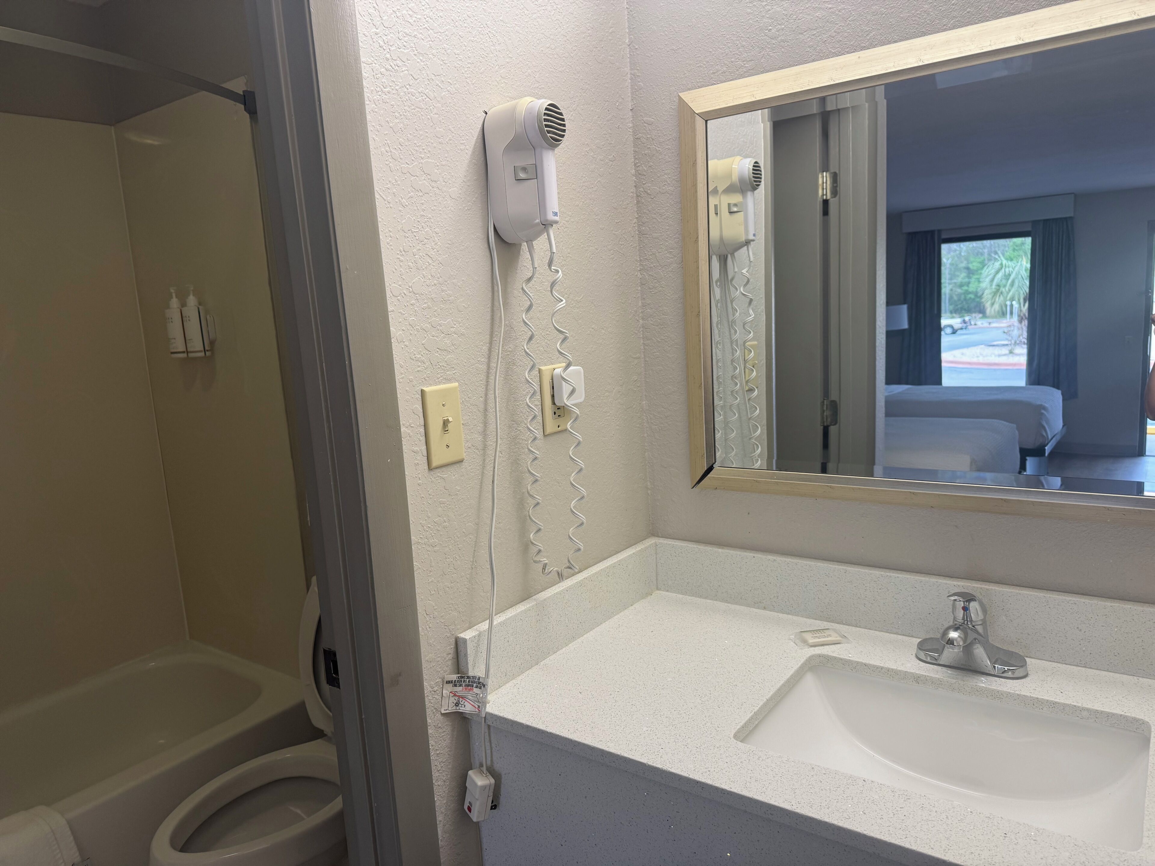 A bathroom with a sink, mirror, and hairdryer mounted on the wall.
