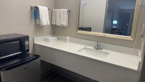 Un baño con lavamanos, espejo, toallero y un microondas.