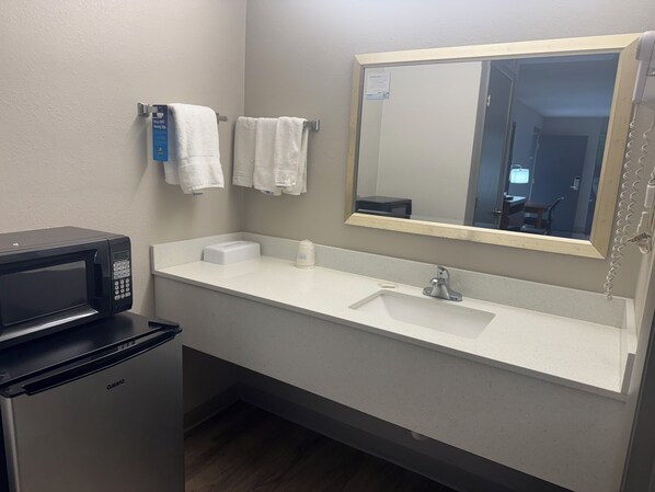 A bathroom with a sink, mirror, towel rack, and a microwave.