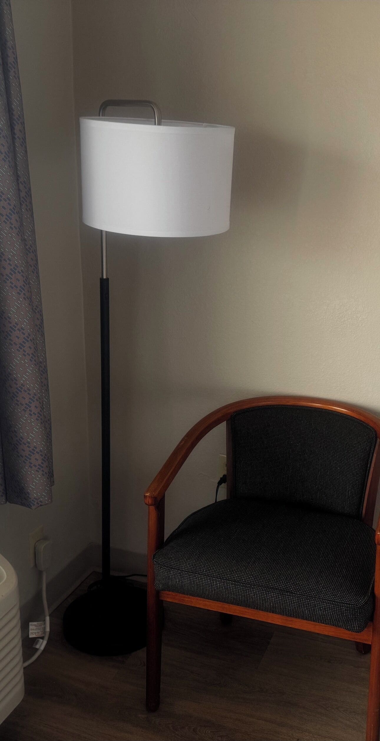 Une pièce d’angle avec un lampadaire, une chaise et un rideau.