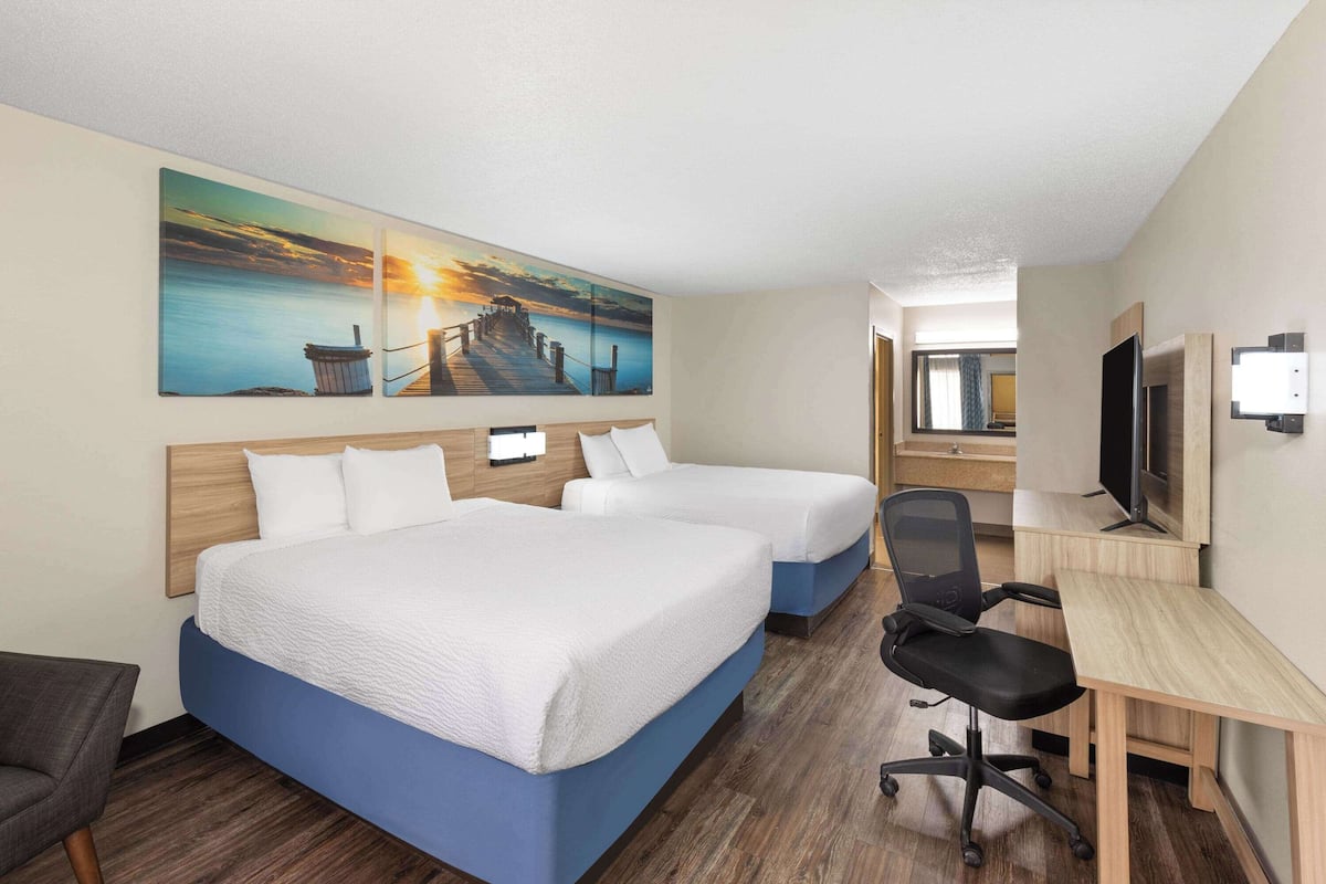 Ein Hotelzimmer mit zwei Betten, einem Schreibtisch, einem Stuhl und einem Fernseher.
