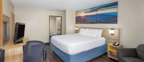 A hotel room with a bed, a desk with a computer, a chair, a couch, and a painting on the wall.