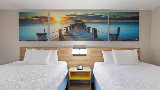 A hotel room with two beds, a wooden headboard, a nightstand with a phone, and a sunset painting above the beds. - Days Inn by Wyndham Oak Grove/Ft. Campbell (Oak Grove)