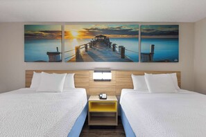 Une chambre d’hôtel avec deux lits, une tête de lit en bois, une table de chevet avec un téléphone et un tableau représentant un coucher de soleil au-dessus des lits.