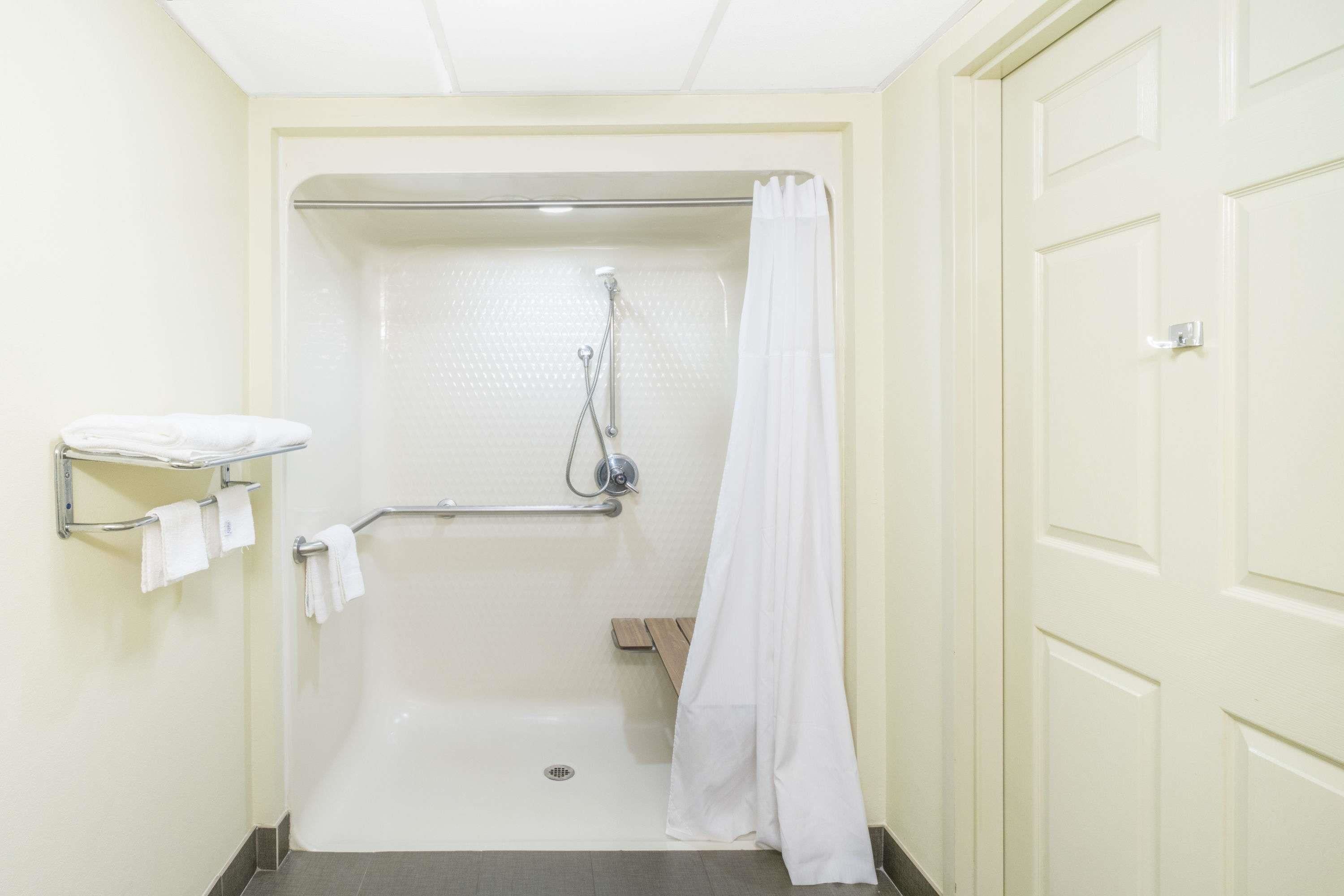 A small, enclosed shower area with a white shower curtain, a towel rack with towels, and a wooden bench.