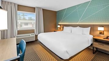 A hotel room with a large bed, a desk, a chair, a nightstand, and a wall-mounted lamp.