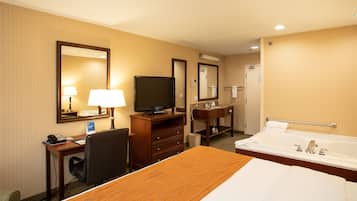 A hotel room with a bed, a desk with a computer, a television, a bathroom with a bathtub, and a mirror.