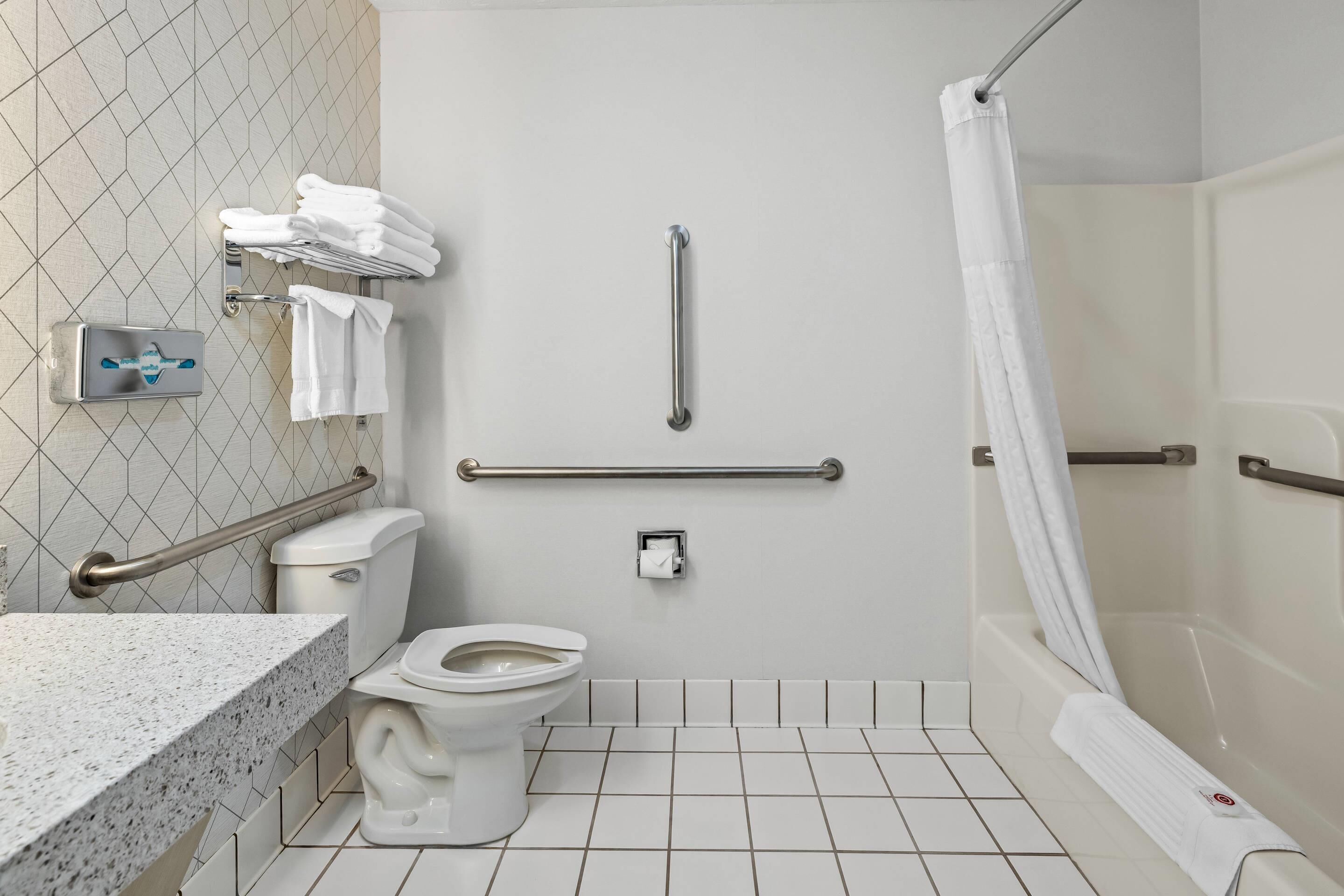 A bathroom with a toilet, grab bars, a shower with a curtain, and a towel rack with towels.