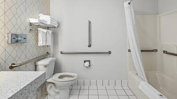 Ein Badezimmer mit Toilette, Haltegriffen, einer Duschkabine und einem Handtuchhalter mit Handtüchern.