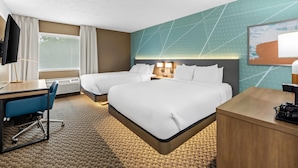 Ett hotellrum med två sängar, ett skrivbord, en stol, en TV och ett stort fönster.