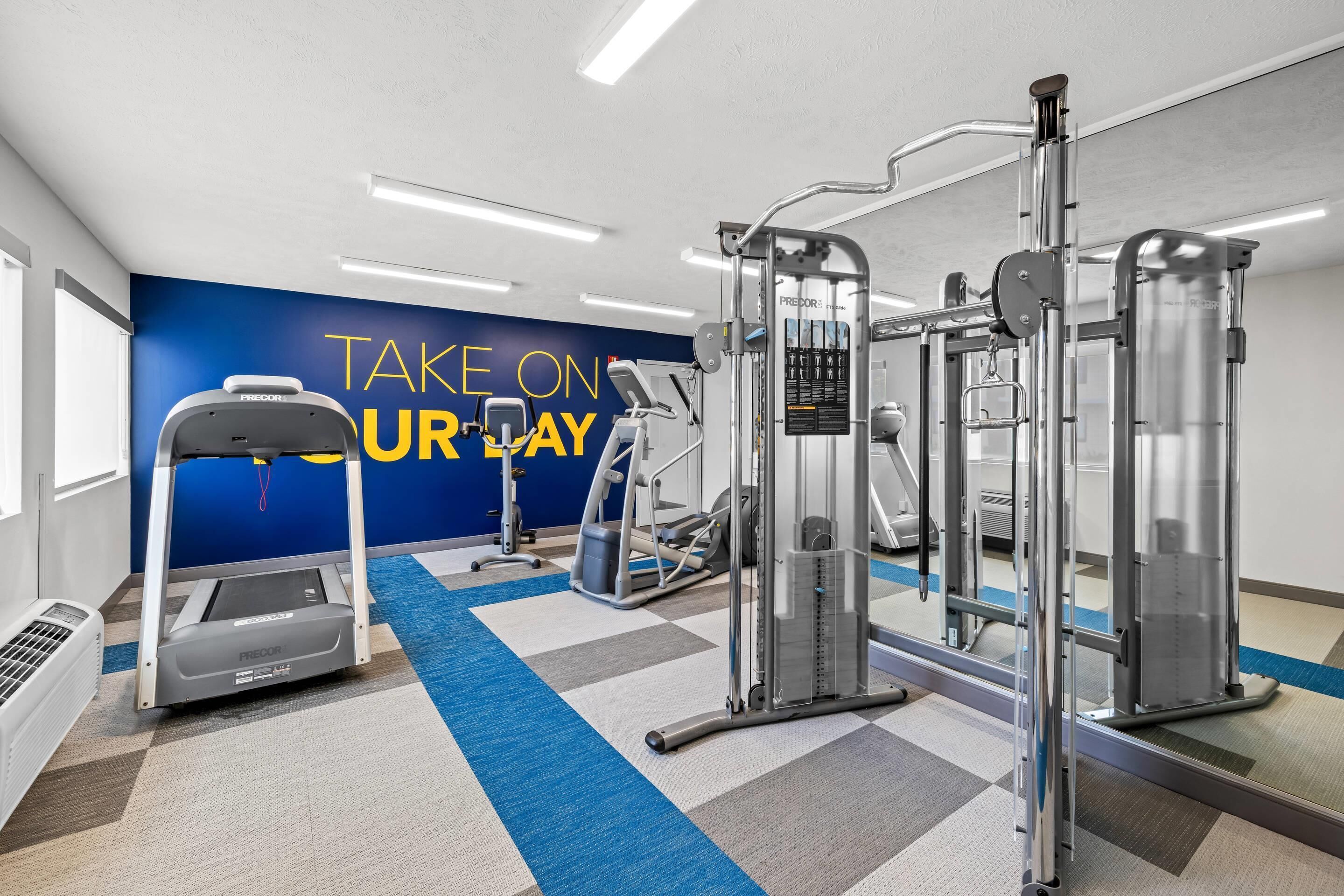 A gym with various exercise equipment, a blue wall with motivational text, and a patterned floor.