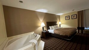 Habitación de hotel con una bañera grande, una cama con dos almohadas, una mesita de noche y una lámpara fijada a la pared.