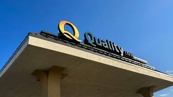 Un letrero de hotel con el nombre 'Quality Inn by Choice Hotels' sobre un cielo azul despejado.