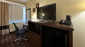 Habitación de hotel con escritorio, televisión, cafetera, silla y ventana con cortinas.