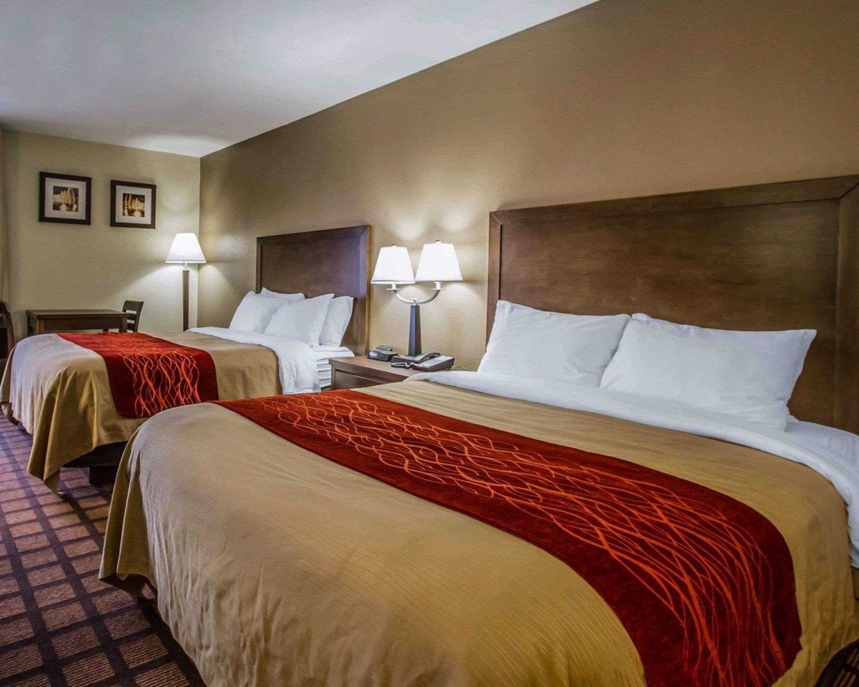 A hotel room with two beds, each with a headboard, bedside tables with lamps, and a check-in counter.