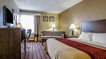 Una habitación de hotel con una cama, un escritorio con computadora, una silla, un sofá y un televisor.