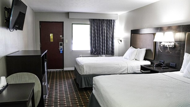 A hotel room with two beds, a desk, a chair, a TV, and a window with curtains. - Days Inn by Wyndham Little River (Little River)