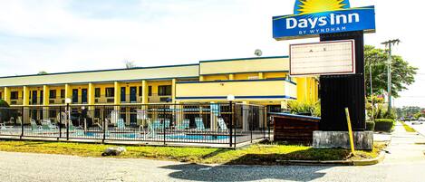 A Days Inn hotel with a swimming pool, outdoor seating, and a clear sky.