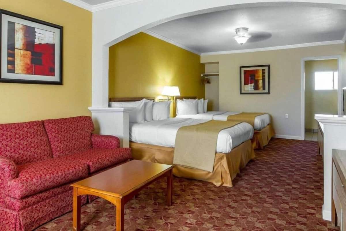 Ein Hotelzimmer mit einem roten Sofa, einem Bett mit beiger Bettdecke, einem kleinen Tisch und einer Deckenleuchte.