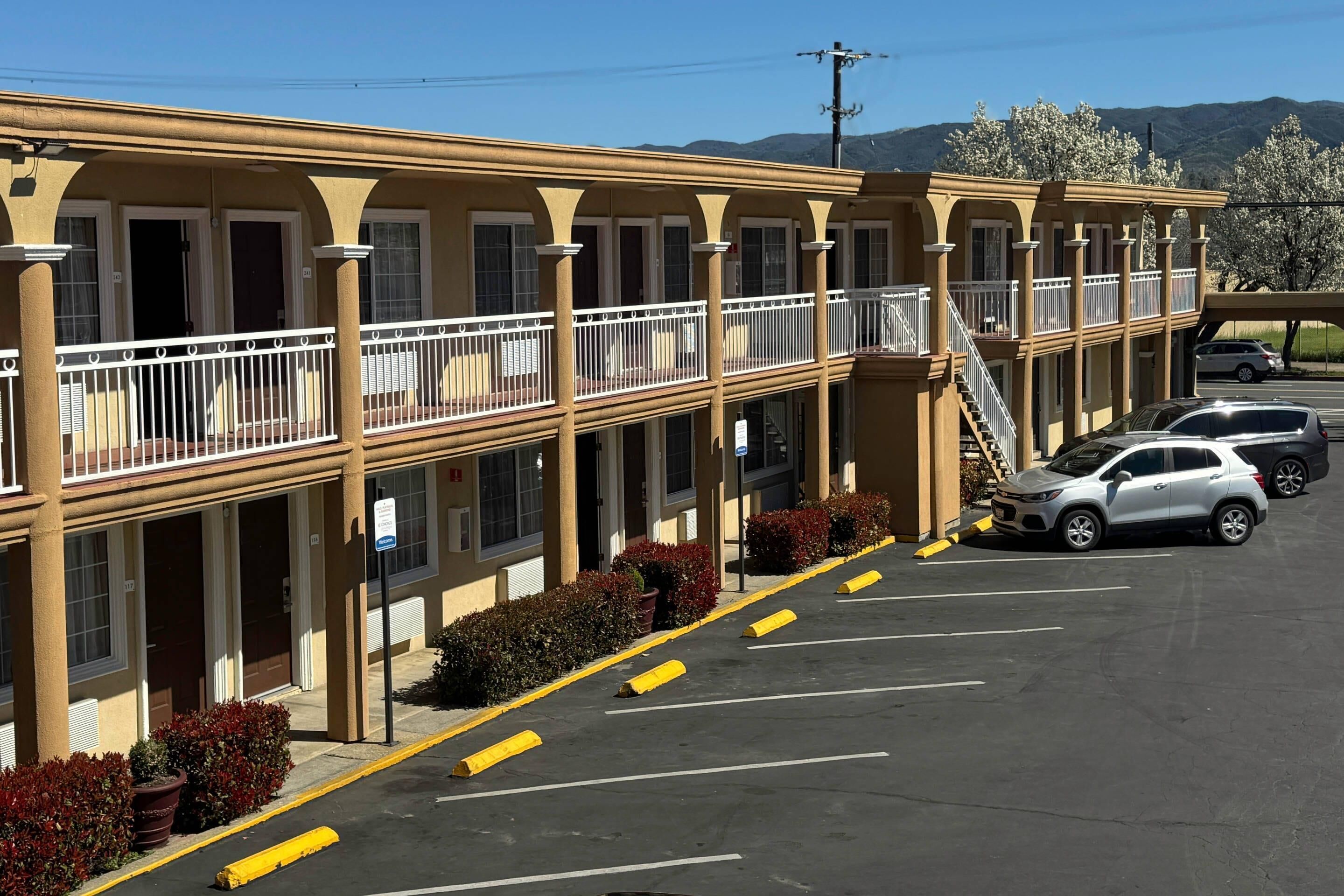 A motel with multiple balconies, a parking lot, and a mountainous backdrop.