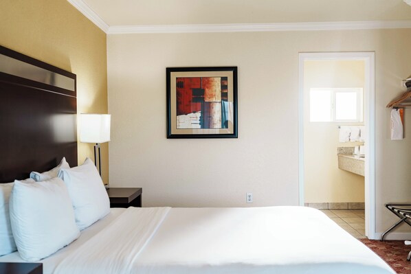 Habitación de hotel con una cama grande, una mesita de noche, un cuadro abstracto enmarco y vistas al baño.
