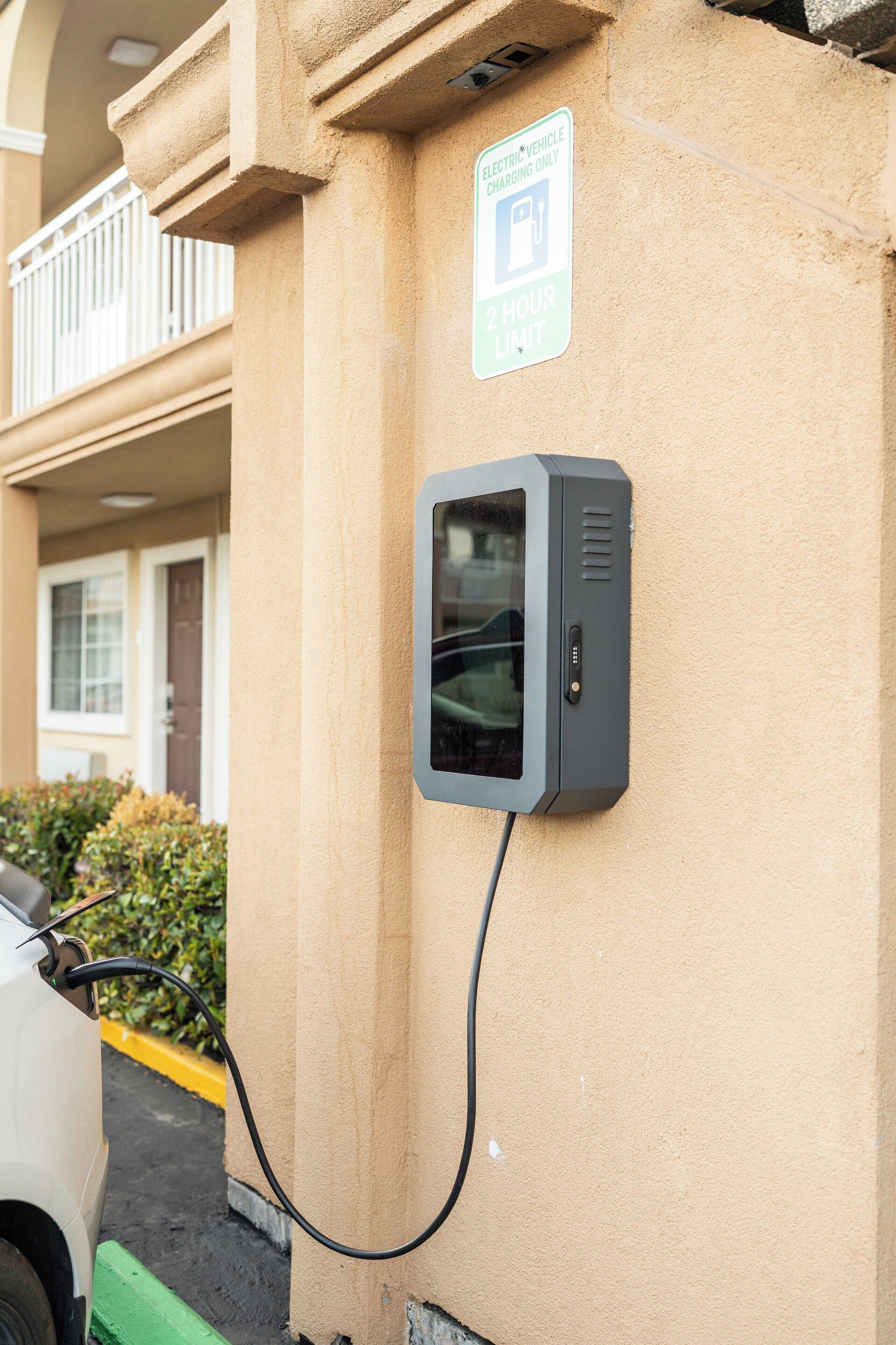 Une borne de recharge pour véhicules électriques fixée sur un mur d’immeuble, avec un panneau indiquant une durée de stationnement maximale de 2 heures.