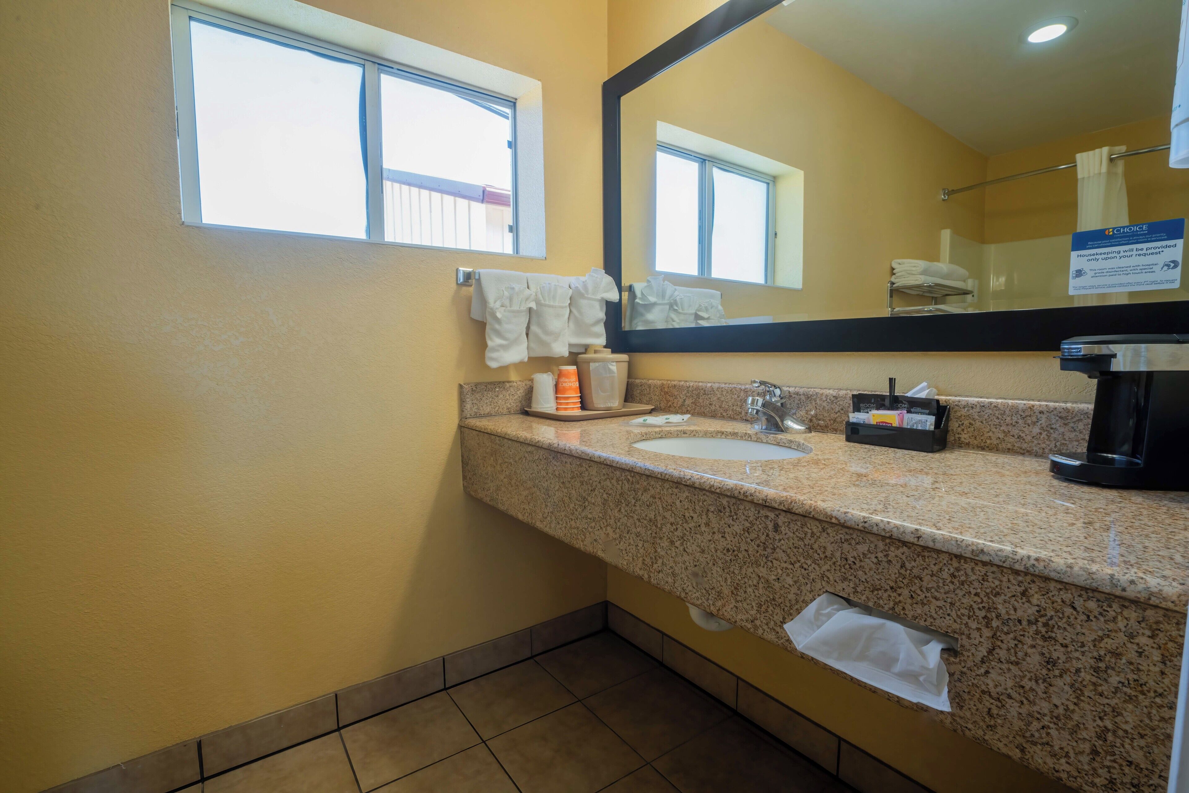 A bathroom with a granite countertop, two sinks, a mirror, and a window.