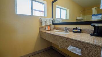 A bathroom with a granite countertop, two sinks, a mirror, and a window.