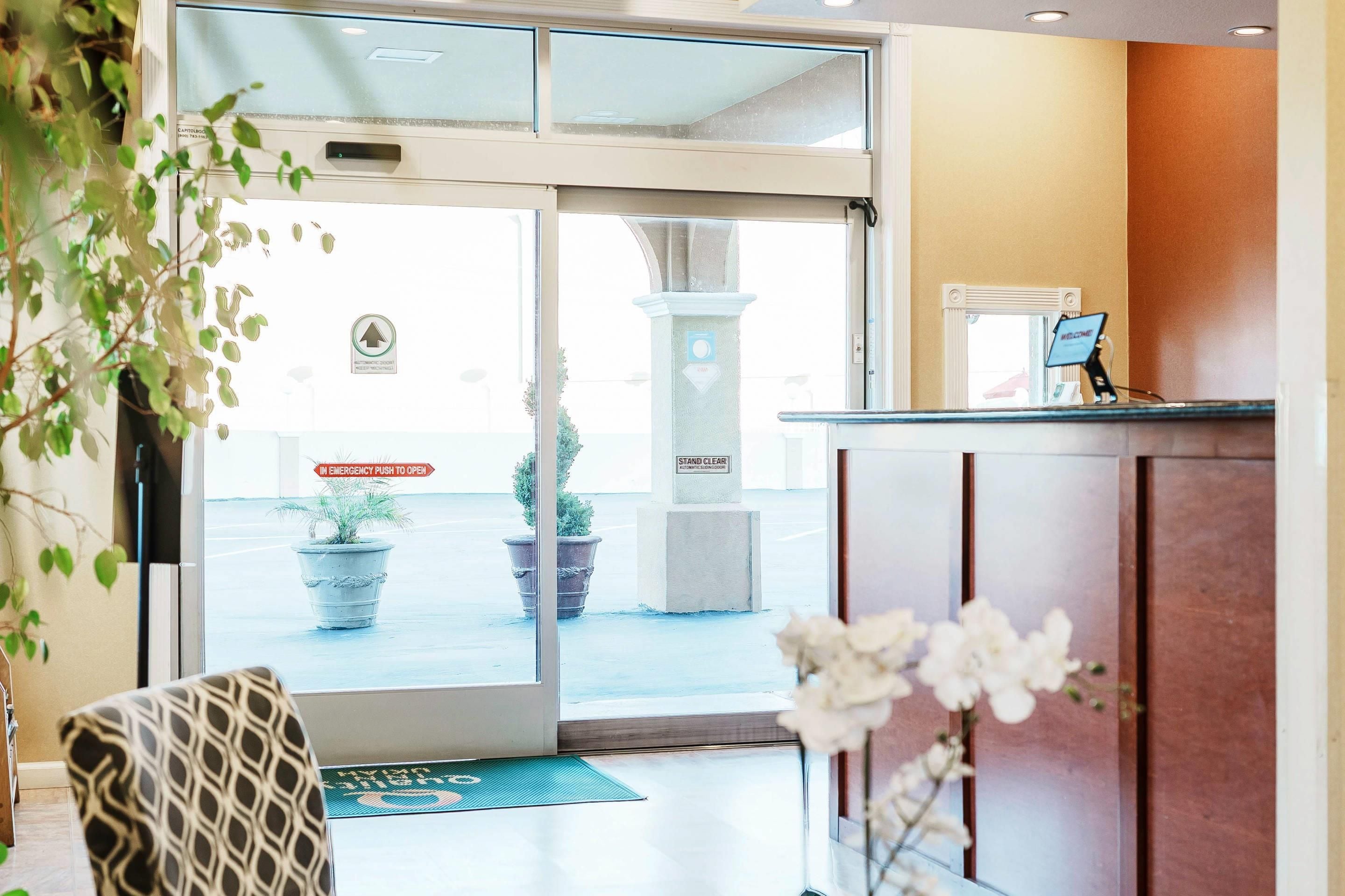 A hotel reception area with a glass door, a reception desk, and potted plants.