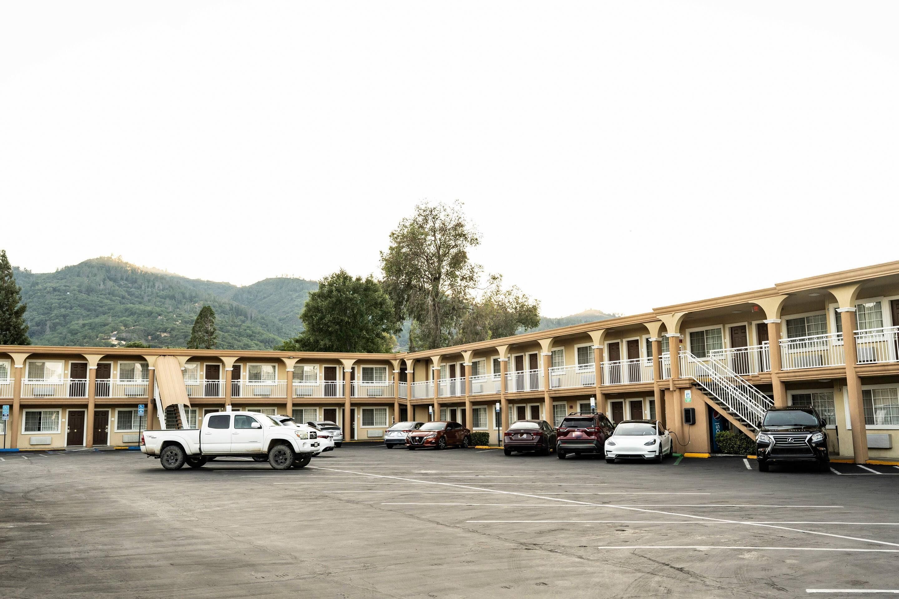 A motel with multiple balconies, a parking lot, and a mountainous backdrop.
