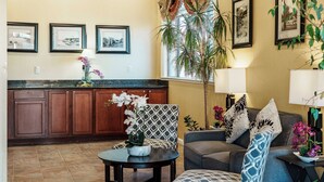 A spacious living area with a sofa, armchairs, a coffee table, and a dining table. There are framed pictures on the wall, a large window with curtains, and a potted plant. - Quality Inn Ukiah (Ukiah)