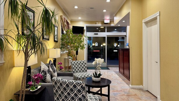A hallway with patterned seating, potted plants, and a reception area with a door and exit sign. - Quality Inn Ukiah (Ukiah)