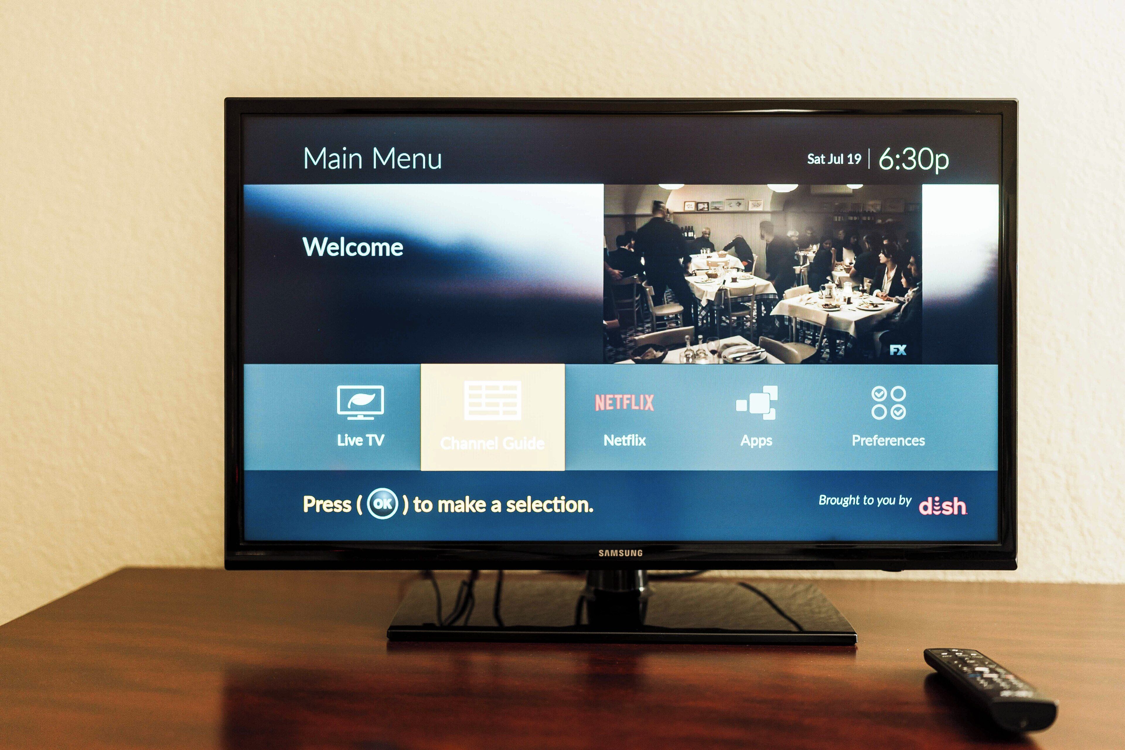A television screen displaying a menu with options like Live TV, Netflix, and Channel Guide, with a remote control on the table.