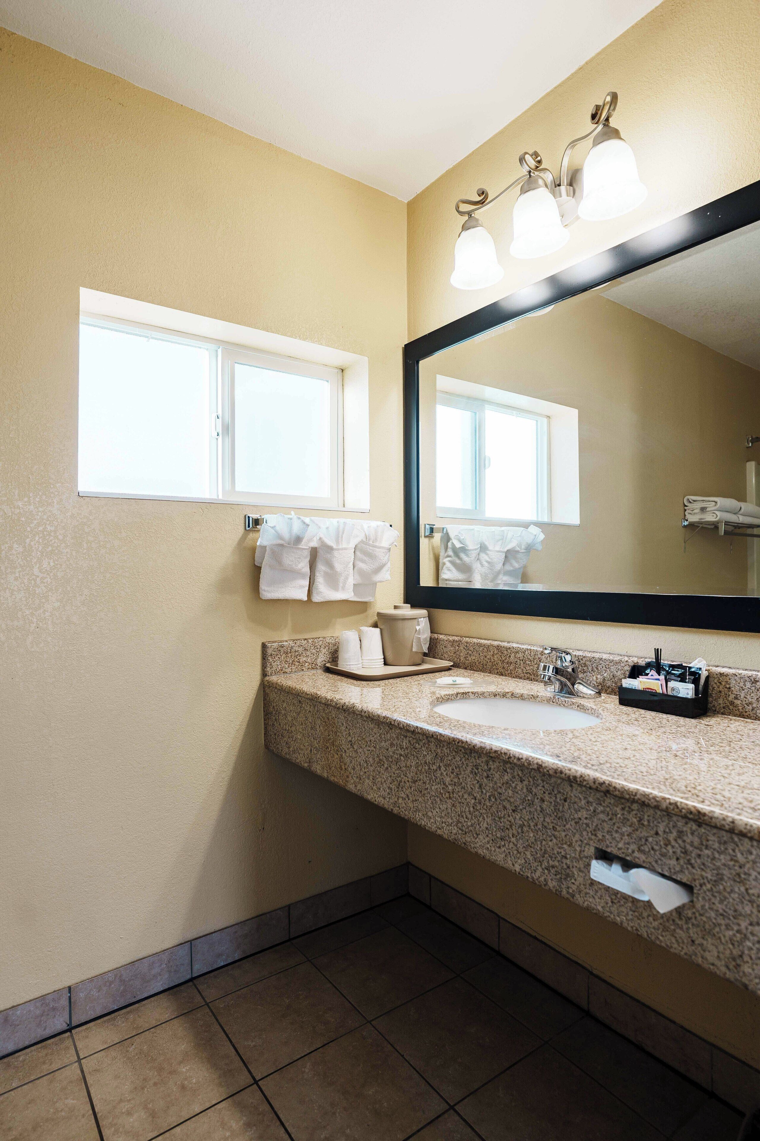 A bathroom with a granite countertop, a large mirror, and a window above the sink.