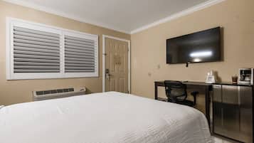 Habitación de hotel con cama, escritorio con cafetera, televisión y puerta con un letrero.