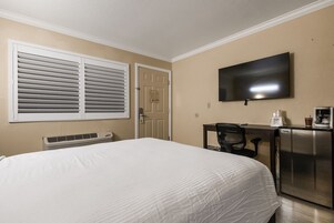 Habitación de hotel con cama, escritorio con cafetera, televisión y puerta con un letrero.