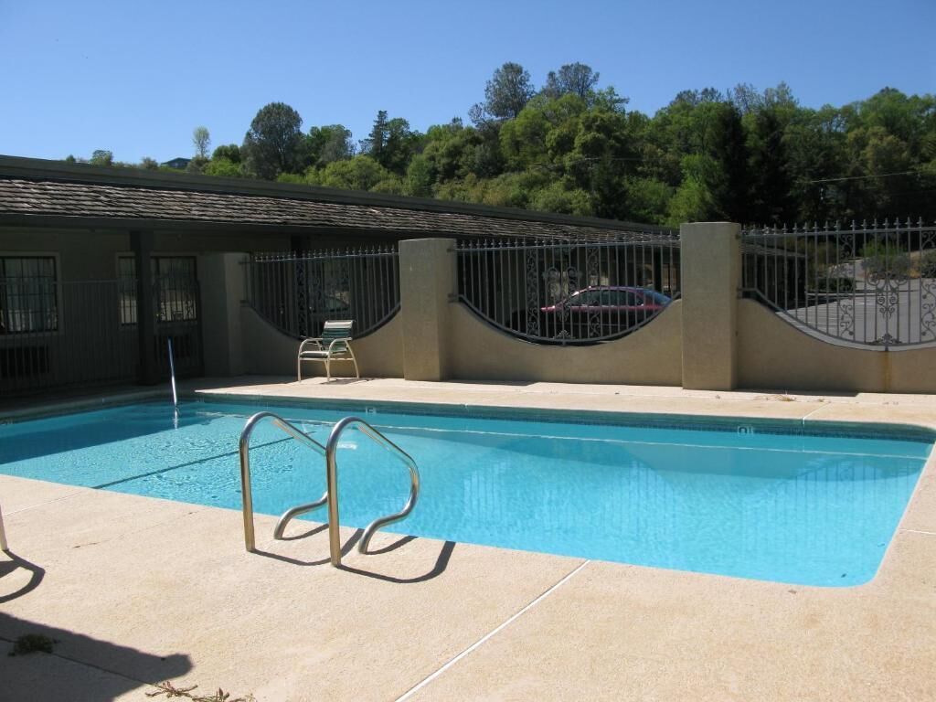 A swimming pool with a metal fence, a covered area, and a car parked nearby.